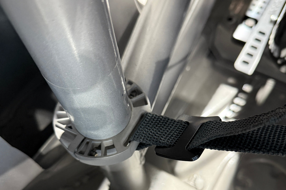 Close-up of a black webbing strap with a plastic buckle attached to a silver metal frame component.